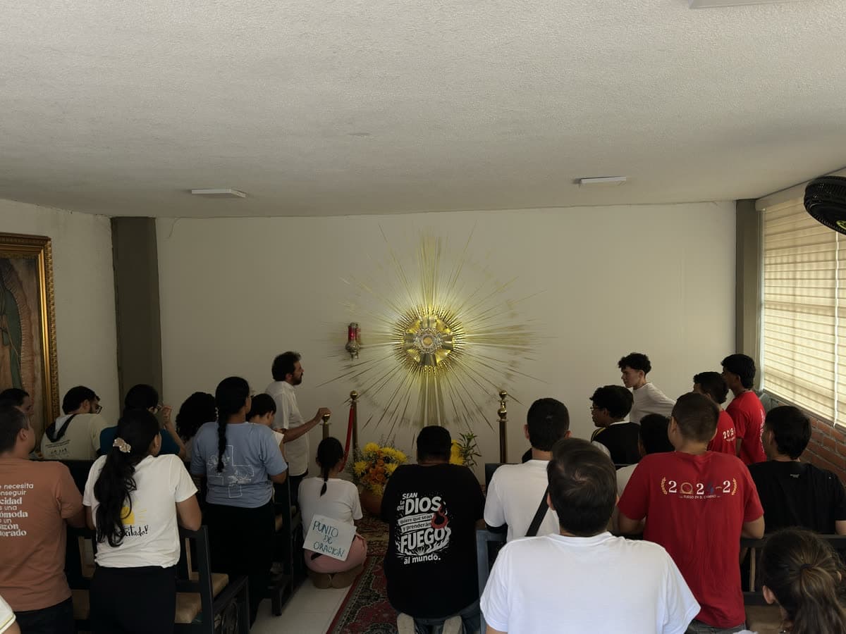 La capilla durante la adoración: la custodia dorada en el centro del muro, y el grupo de jóvenes sentados y de pie, de espaldas, mirando hacia ella.